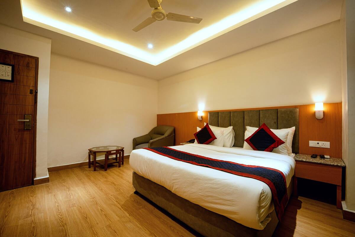 A hotel room with a large bed, a wooden headboard, a small table, a chair, and a ceiling fan.