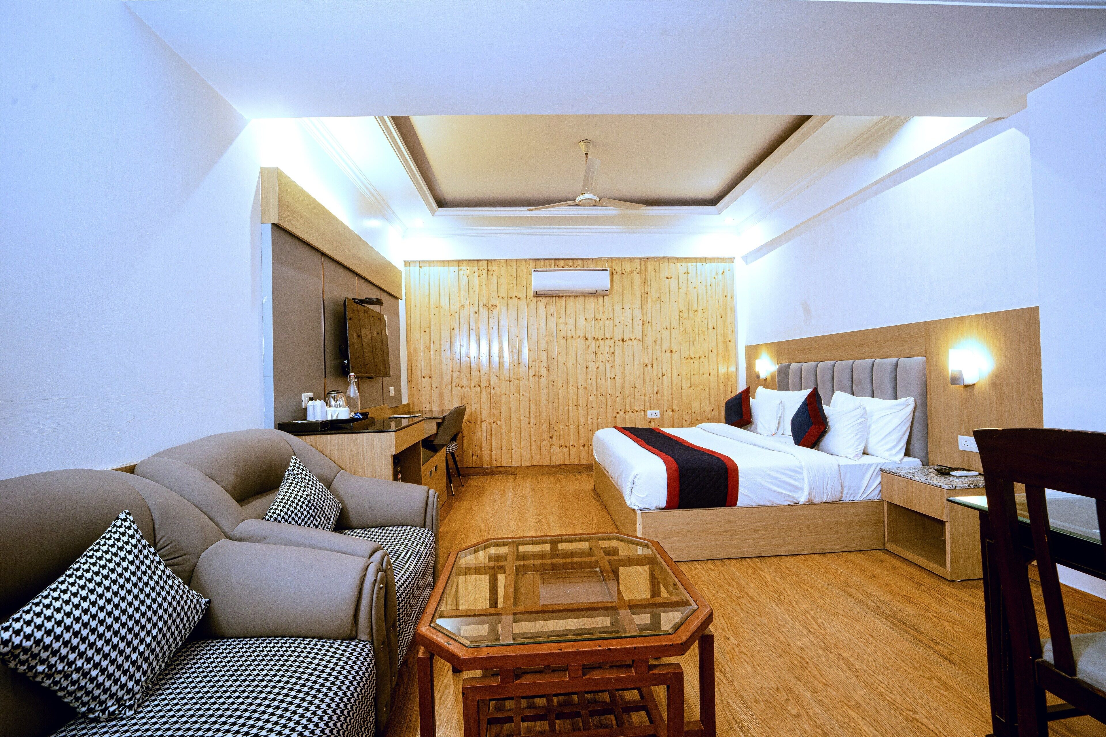 Habitación de hotel con cama, sofá, mesa de vidrio, escritorio y silla.