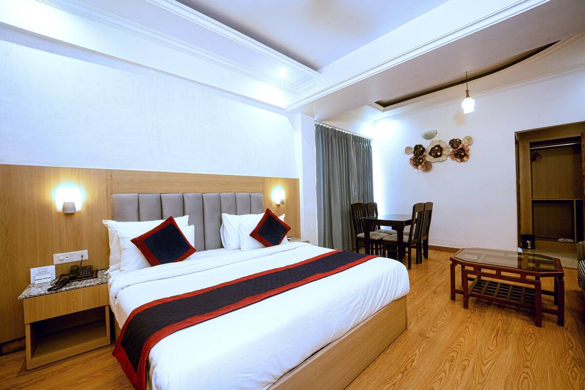 A hotel room with a large bed, a wooden nightstand, a glass table, and a seating area with chairs.