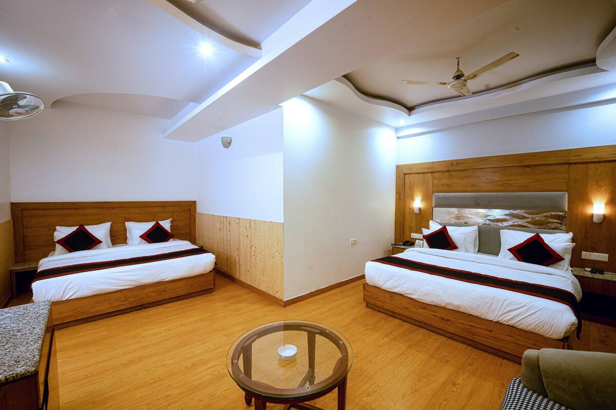 A hotel room with two beds, a small table, and a ceiling fan.