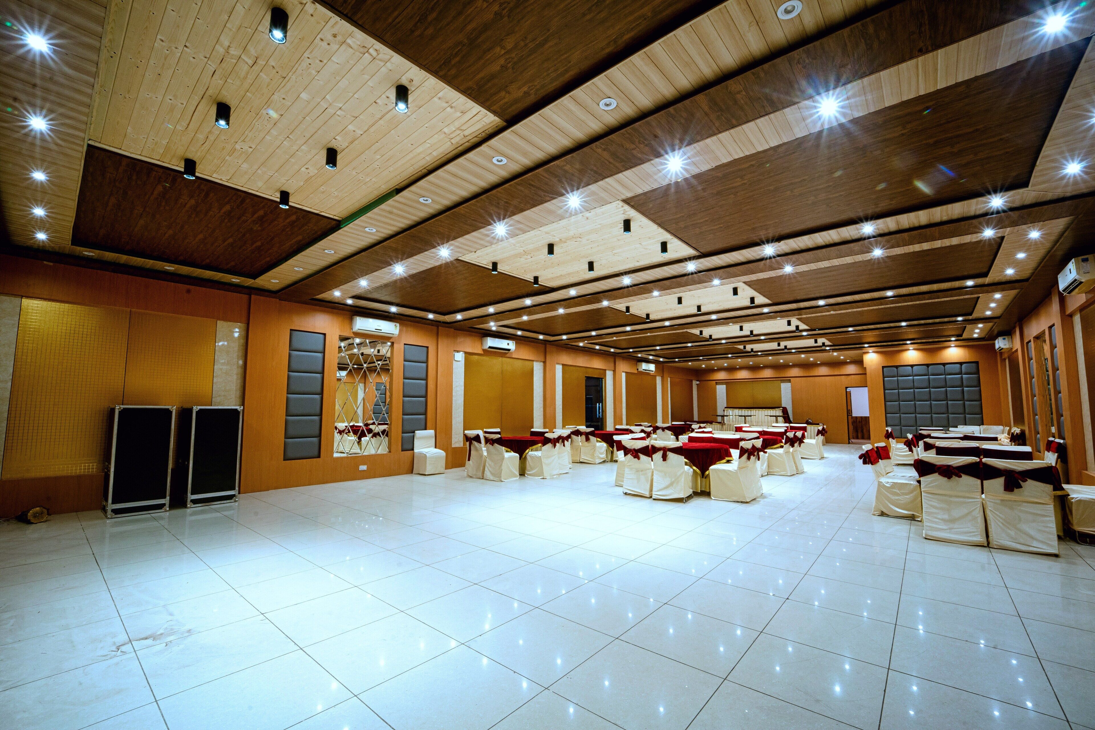 Un amplio salón de banquetes con varias mesas y sillas, techo de madera con iluminación empotrada y suelo de baldosas.
