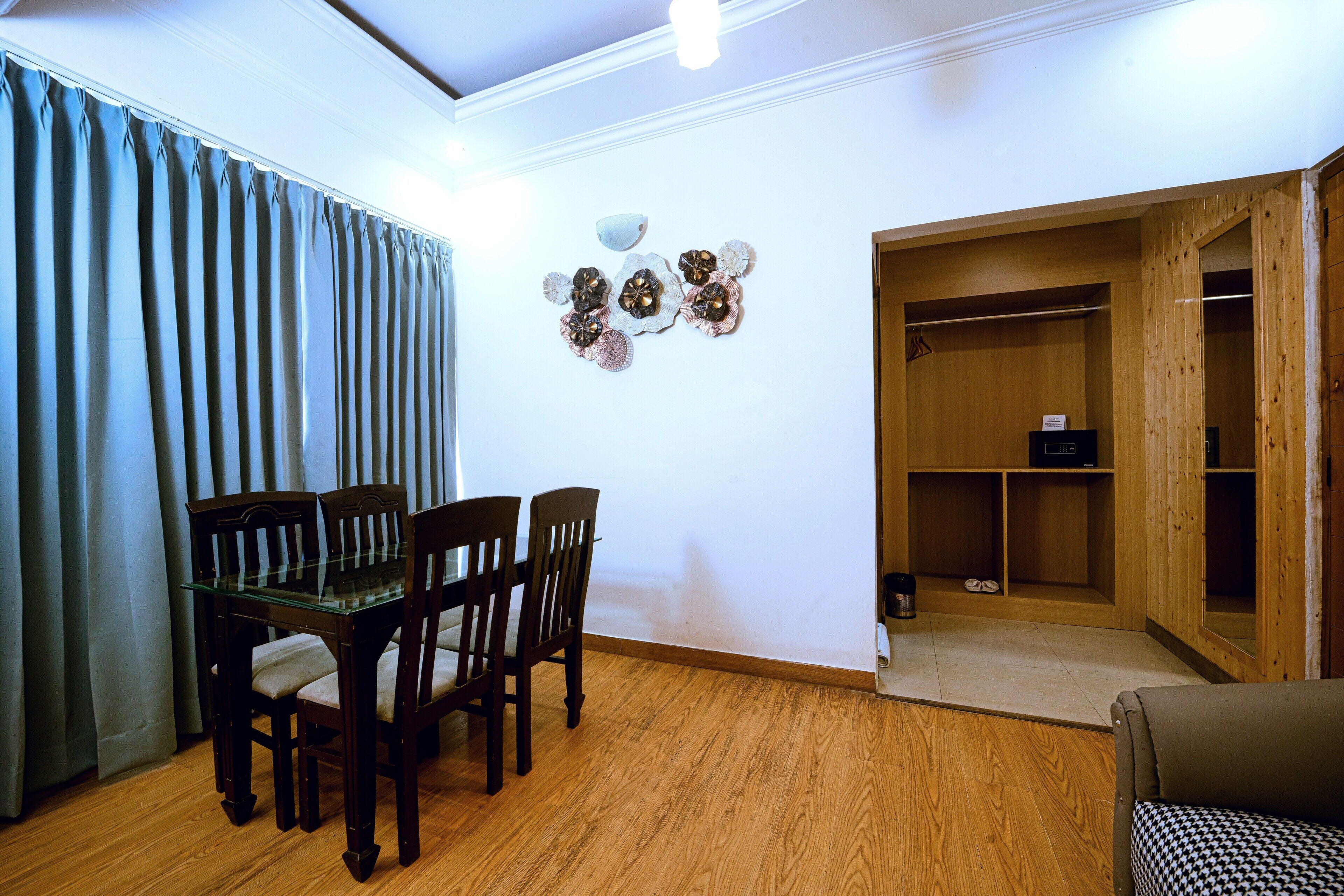 Un comedor con mesa de vidrio y sillas de madera, piso de madera, pared decorada con placas y armario de madera con estantes.