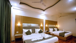A hotel room with two beds, wooden headboards, wall-mounted lights, a ceiling fan, and a wooden floor. - Grand Legacy Beacon Dehradun (Dehradun)