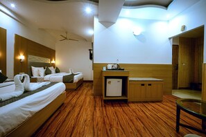 Une chambre d’hôtel avec deux lits, un petit réfrigérateur, une armoire en bois, un ventilateur de plafond et une table en verre.