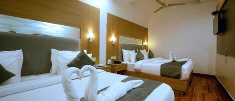 A hotel room with two beds, wooden headboards, wall-mounted lights, a ceiling fan, and a flat-screen TV.