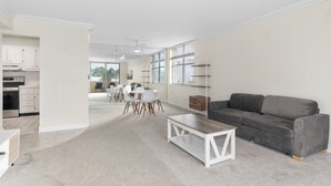 Ein geräumiges Wohnzimmer mit grauem Sofa, einem weißen Couchtisch und einem Essbereich mit weißen Stühlen und einem Tisch.