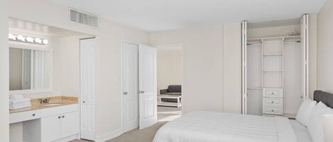 A bedroom with two beds, a vanity with a mirror and lights, a closet, and a chair in the background.