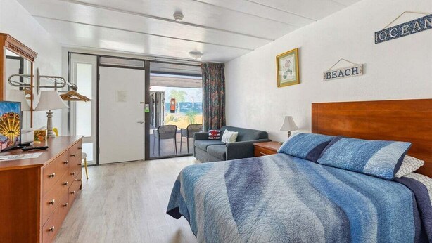 Een hotelkamer met een bed, een bureau, een stoel, een dressoir en een schuifdeur naar buiten.