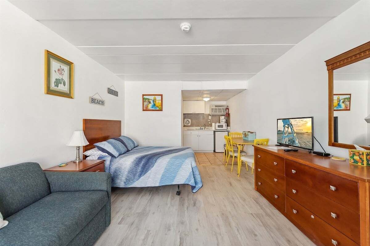 Ein kleines Zimmer mit einem Bett, einer Schlafcouch, einer Holzkommode, einem Schreibtisch und einem Stuhl.