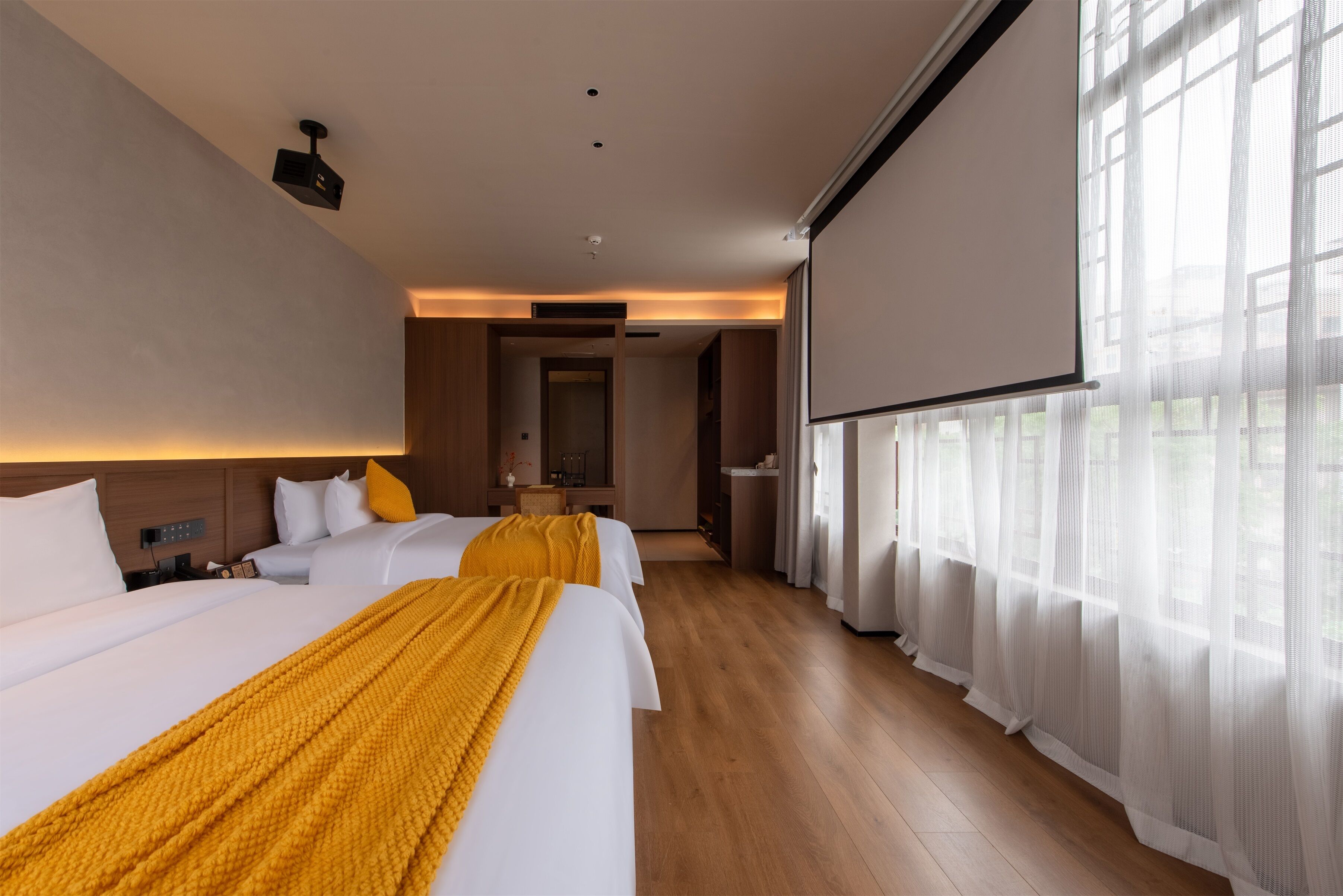 A hotel room with two beds, a projector, and a large window with sheer curtains.