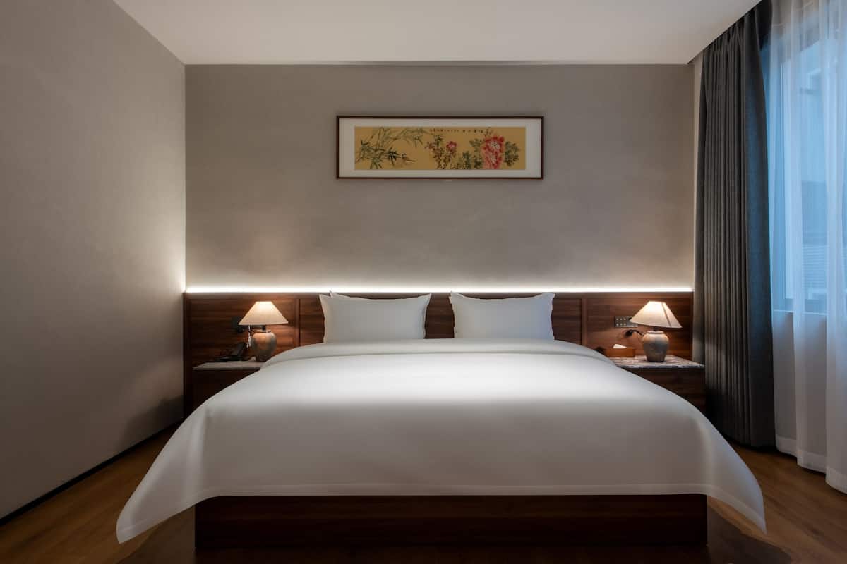 Ein modernes Hotelzimmer mit einem großen Bett, einem Holz-Kopfteil, zwei Nachttischlampen und einem gerahmten Kunstwerk an der Wand.