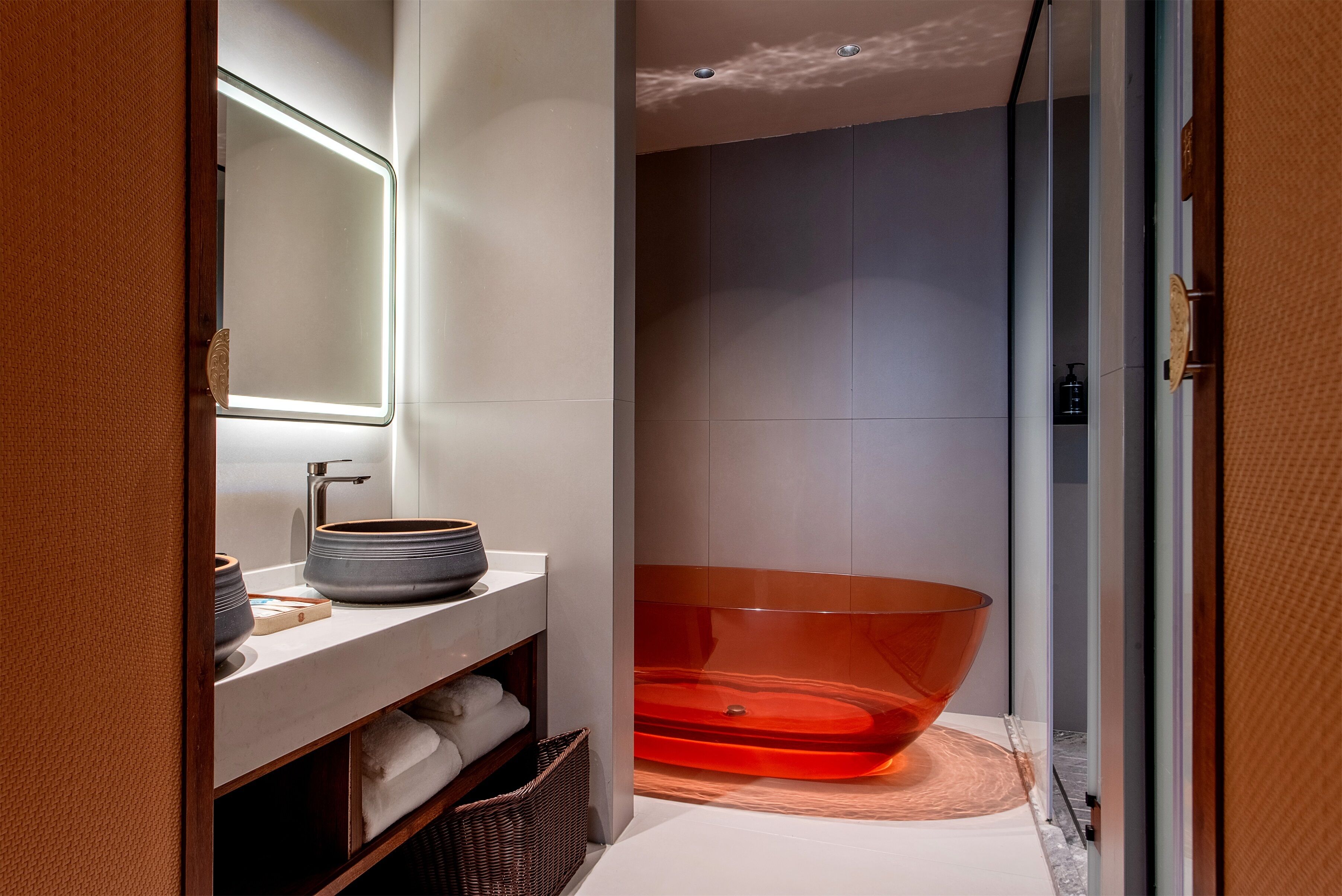 A modern bathroom with a large mirror, a white countertop, a bathtub, and a wicker basket.