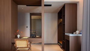 Una habitación de hotel moderna con una cama, un escritorio, una silla, un armario y un baño visible a través de una puerta de cristal.