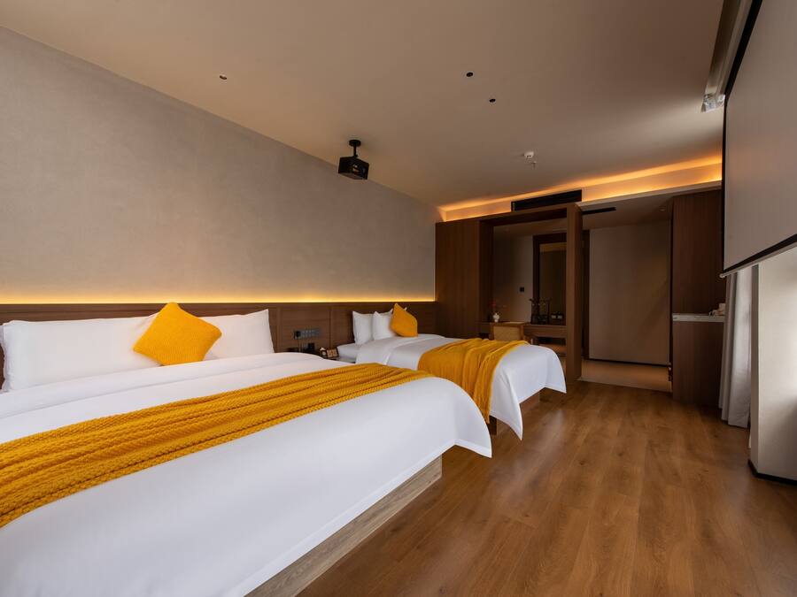 Habitación de hotel con dos camas, piso de madera, una lámpara de techo moderna y una puerta que da a otra habitación.