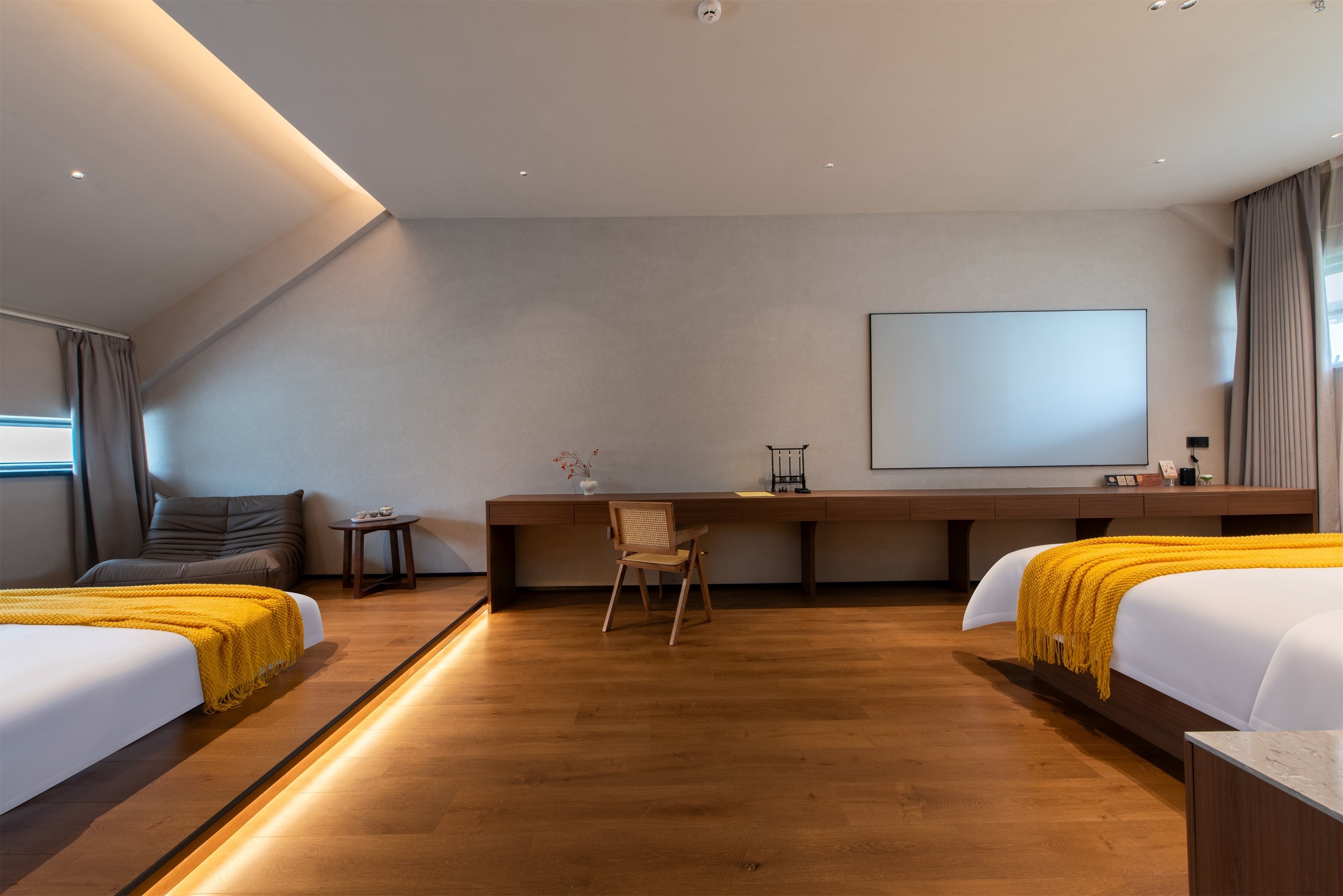 A modern hotel room with two beds, a desk, a chair, and a large screen.