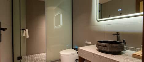 A modern bathroom with a glass shower enclosure, a white toilet, a marble sink, and a mirror with integrated lighting.