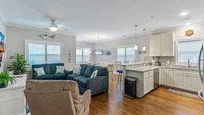 A modern living room with a sofa, a dining area, and a kitchen with white cabinets and a countertop. - Residence 304S at The Sandcastle Condominiums (Wildwood Crest)