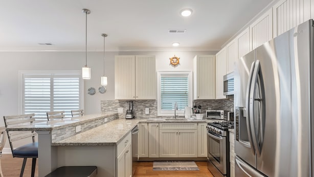 A modern kitchen with a stainless steel refrigerator, granite countertops, and a central island with bar stools. - Residence 304S at The Sandcastle Condominiums (Wildwood Crest)