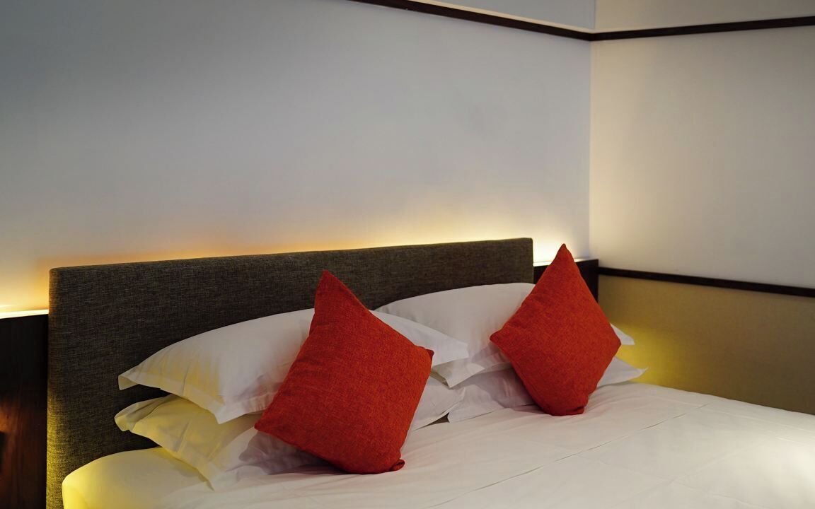 A neatly made bed with white linens and two red pillows.