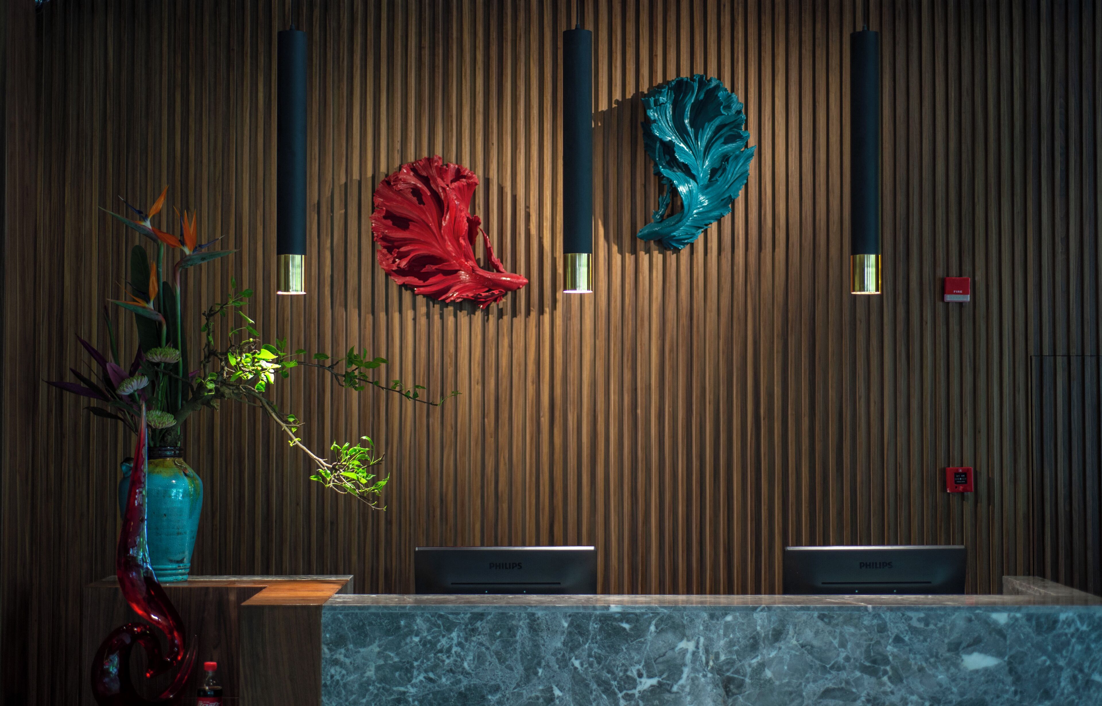 Una recepción con encimera de mármol, dos dispositivos Philips, una escultura abstracta roja y una azul, y un florero azul con una planta.