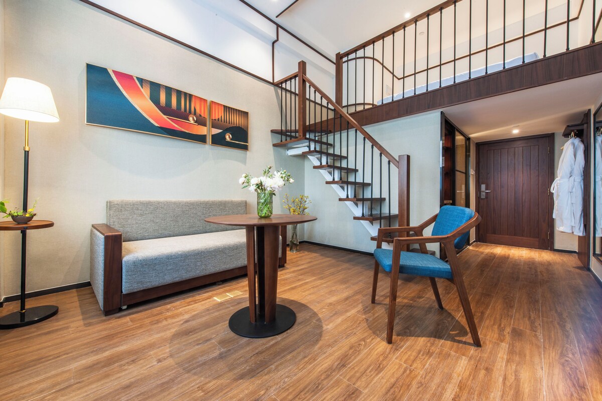 Een modern interieur met een houten trap, een grijze bank, een ronde tafel met een vaas en een blauwe stoel.