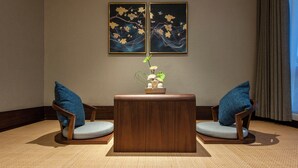Ein Zimmer mit einem runden Holztisch, zwei Stühlen mit blauen Kissen, einer Vase mit Blumen und zwei Bildern an der Wand.