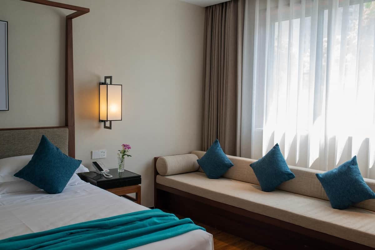 Ein Hotelzimmer mit Bett, Nachttisch, Lampe und einem Fenster mit Vorhängen.