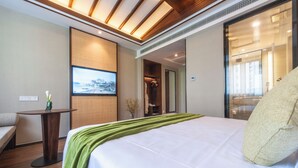 Ein Hotelzimmer mit einem Bett, einem kleinen Tisch mit einer Vase, einem an der Wand montierten Fernseher und einem Schiebetürenschrank.