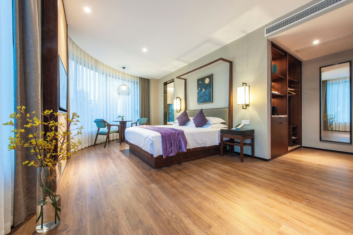 Ein Hotelzimmer mit Bett, Nachttisch, Sessel und einem großen Fenster.