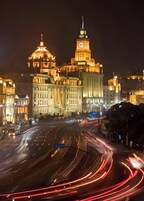 A nighttime cityscape with illuminated buildings and a busy highway with light trails.