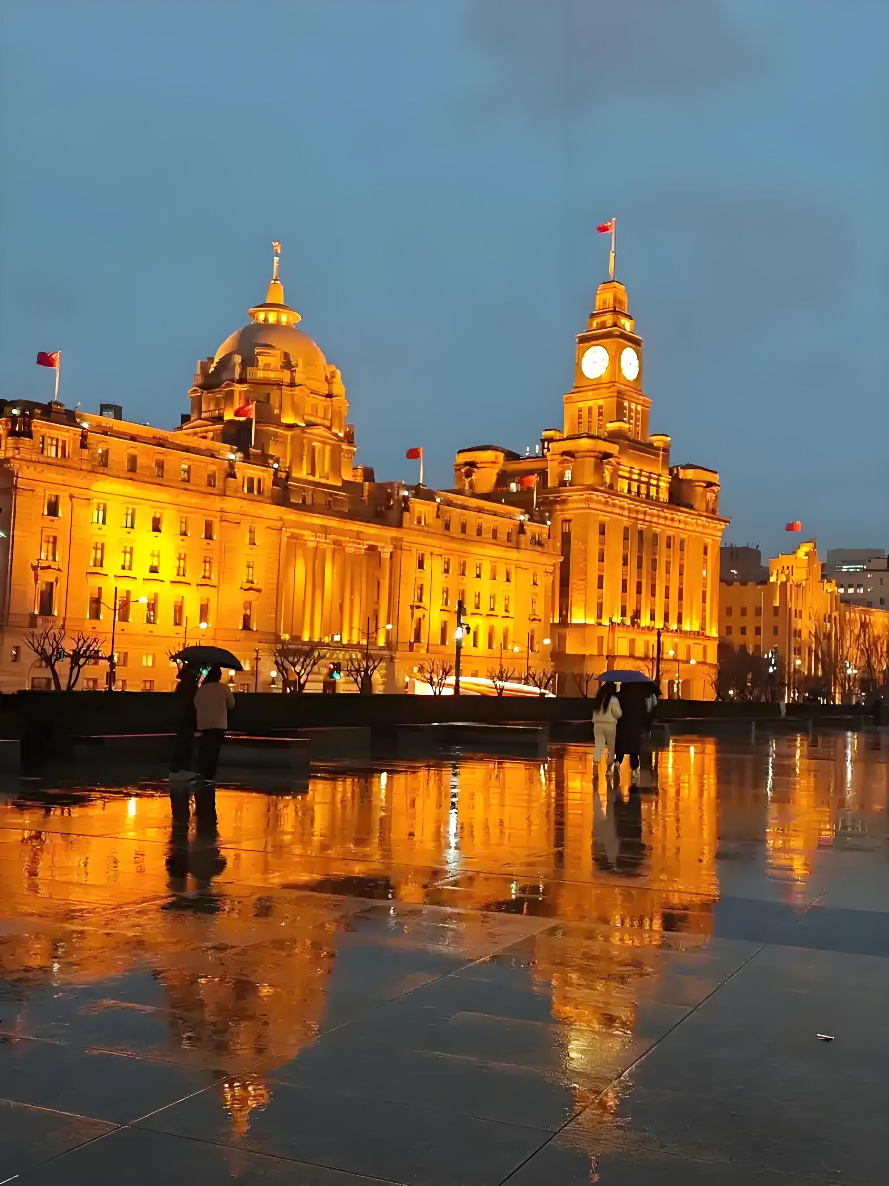 A large, illuminated building with a prominent dome and clock tower, reflecting on a wet surface.