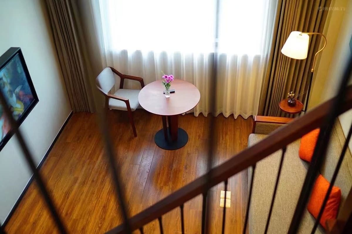 Ein Hotelzimmer mit rundem Tisch, zwei Stühlen, einer Blumenvase, einer Lampe und Blick durch leichte Vorhänge.