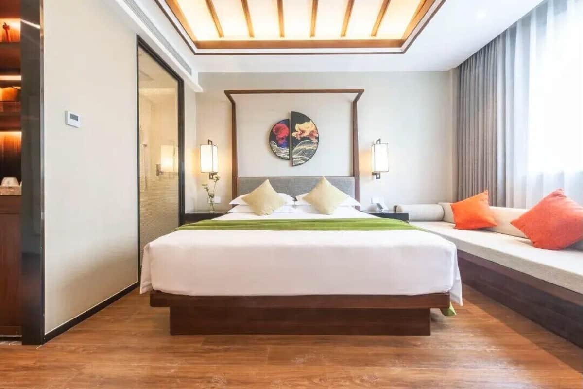 Ein Hotelzimmer mit einem großen Bett, einem Nachttisch, einem Wandbild und einem Fenster mit Vorhängen.