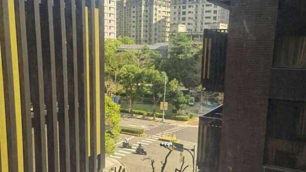 Une vue depuis une fenêtre donnant sur un paysage urbain, avec des bâtiments modernes, un passage piéton et quelques arbres.