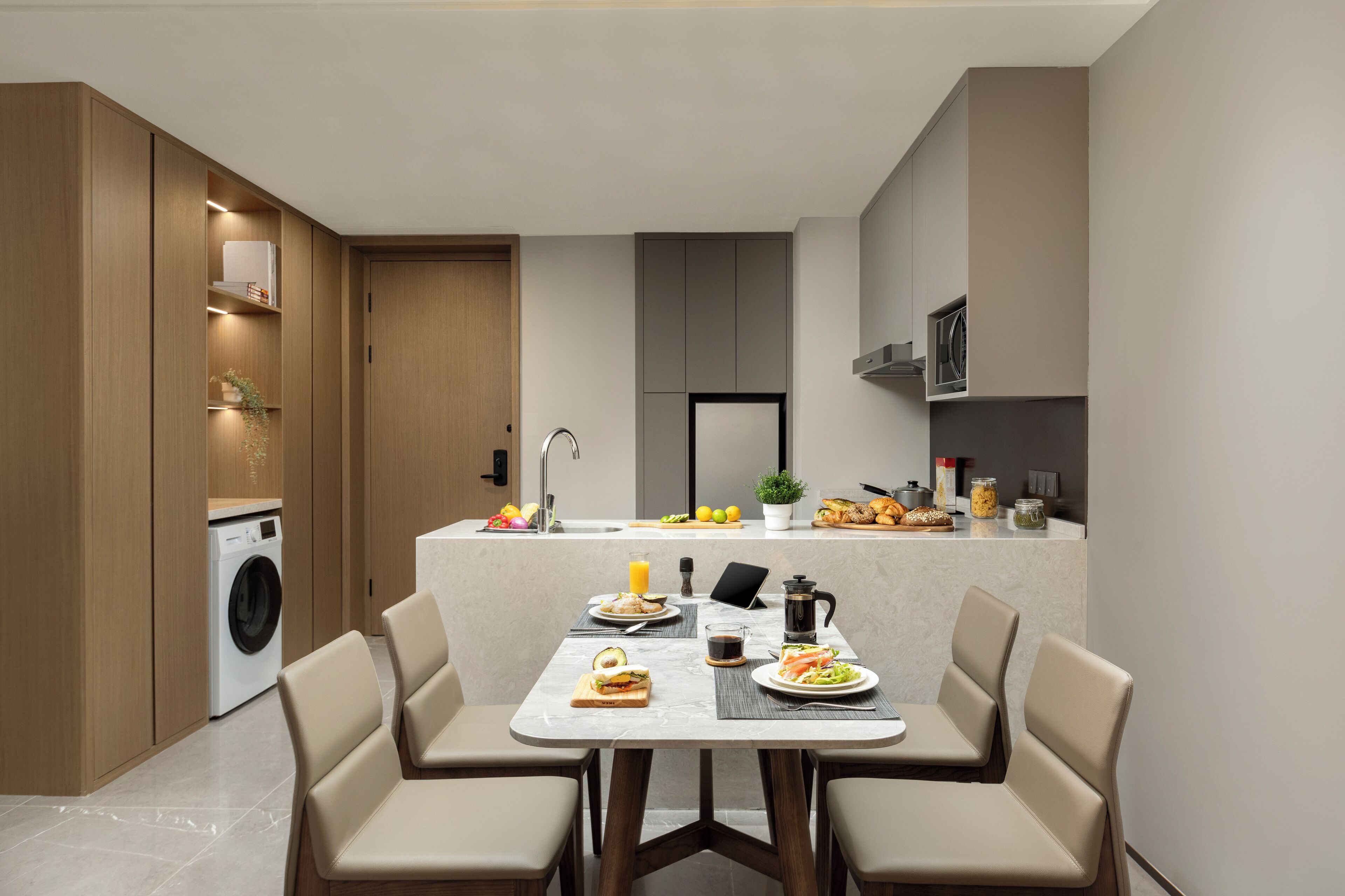 Een moderne keuken met een centraal eiland, geïntegreerde apparatuur en een eethoek met stoelen en een tafel gedekt voor twee personen.