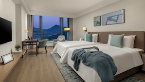 A hotel room with two beds, a desk, a chair, a TV, and a large window with a mountain view. - Qingshan Lake Tianlan Hotel Hangzhou (Hangzhou)