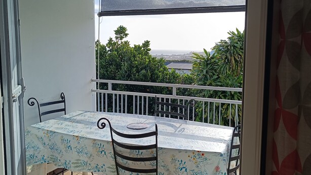 A balcony with a table and chairs, a view of greenery and a distant landscape.