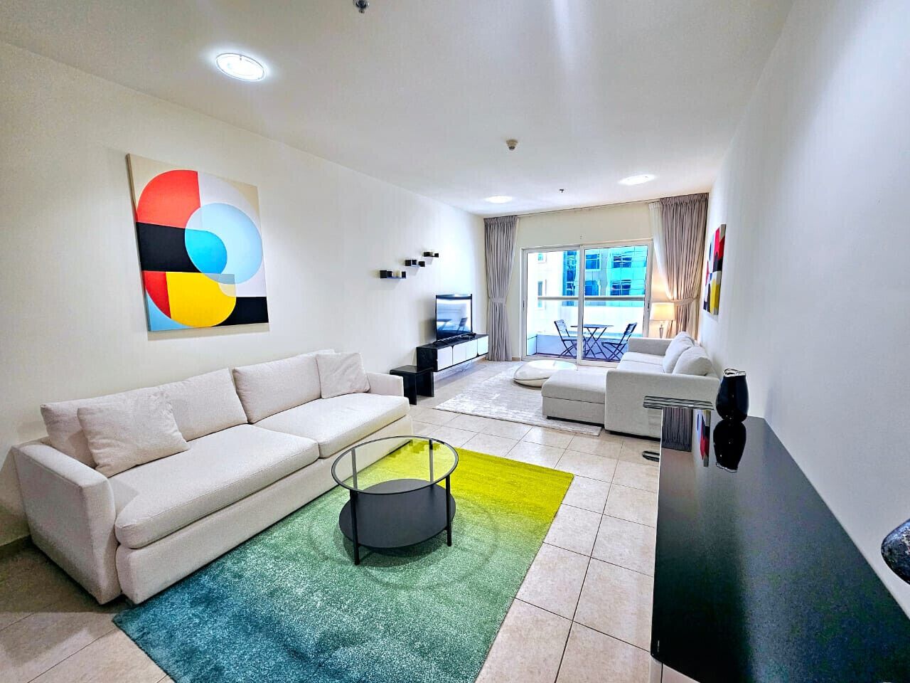 A modern living room with a white sofa, a coffee table, and a colorful abstract painting on the wall.