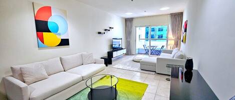 A modern living room with a white sofa, a coffee table, and a colorful abstract painting on the wall.