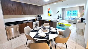 Una cucina moderna con lavastoviglie, zona pranzo con tavolo apparecchiato per quattro persone e soggiorno con divano e tavolino.