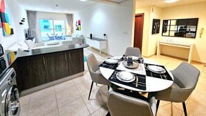 Una cucina moderna con isola centrale, tavolo da pranzo e sedie. Si vede anche un soggiorno con divano e finestra.