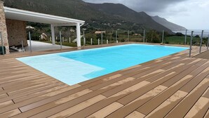 En pool med en träbrygga, ett överbyggt område och en bergig bakgrund.