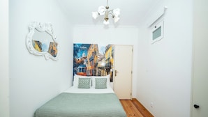 Une chambre à coucher avec un lit, un miroir, un tableau représentant Lisbonne et un lustre.