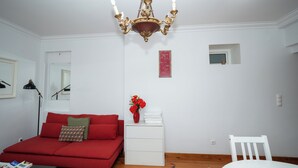 Une pièce avec un canapé rouge, une table de chevet blanche, une chaise blanche et un lustre.