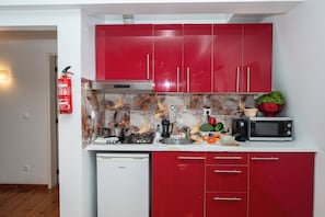 A compact kitchen with red cabinets, a stainless steel range hood, a microwave, and a dishwasher.