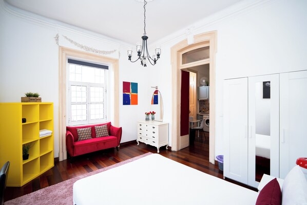 A bedroom with a bed, a red sofa, a white dresser, a yellow bookshelf, and a wardrobe.