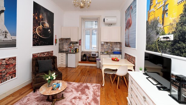 A modern kitchen with white cabinets, a dining area with a table and chairs, a sofa, and a coffee table with books and flowers.