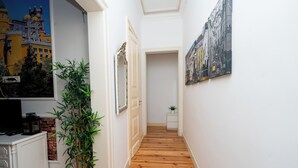 A hallway with wooden flooring, a potted plant, a white cabinet, and artwork on the walls.