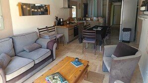 A modern living room with a sofa, a coffee table with books, and a dining area with chairs and a table. - Chanvre - Escape and well-being with a private Jacuzzi (Rosières)