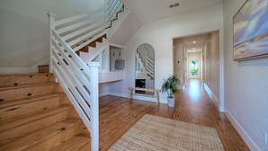 A spacious hallway with wooden flooring, a white staircase, and a bench. - Coastal Escape w/ Pond Views + Pool Access | Graham’s Getaway by AvantStay (Port Aransas)